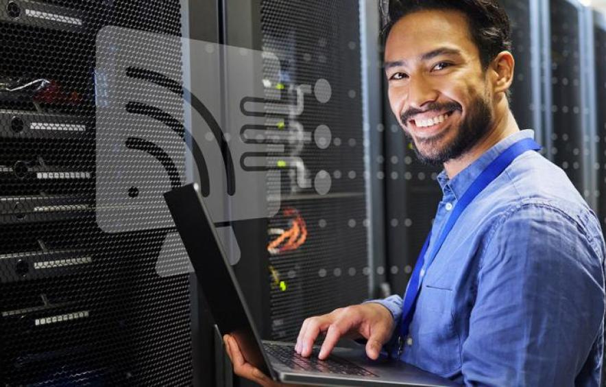 Smiling IT professional working on a laptop in a server room