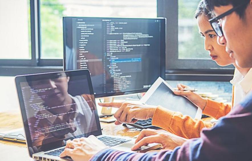 Two people working together on code displayed on laptops and monitors.
