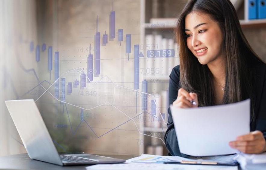 Woman reviewing documents and laptop with overlaid data charts